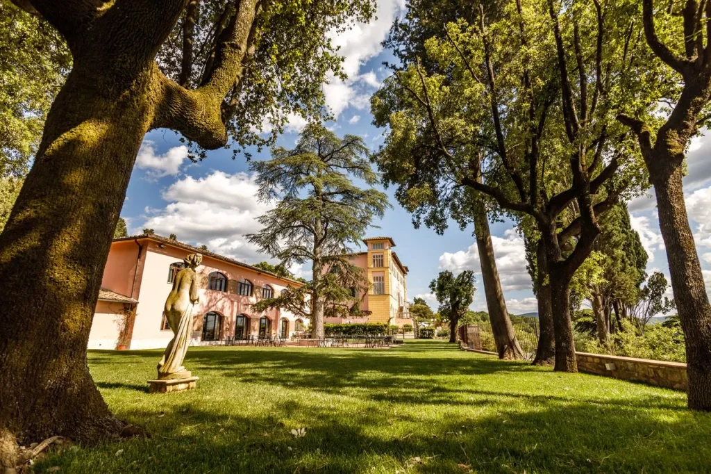 Edificio storico circondato da giardino alberato e statua.