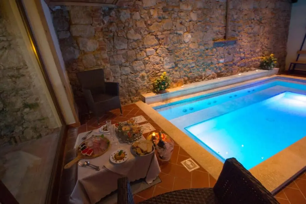 Piscina interna con tavolo apparecchiato e muri in pietra.
