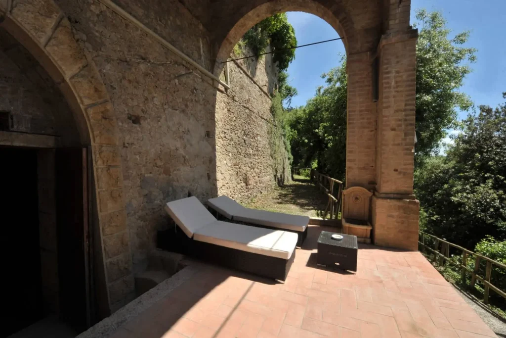 Due lettini su terrazza soleggiata con pareti in pietra.